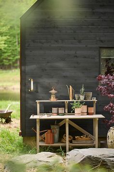 a table with potted plants on it in front of a black building and trees