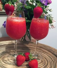 two glasses filled with liquid and strawberries on top of a table next to flowers