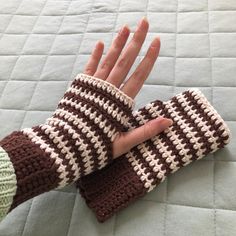 a person's hand wearing a brown and white crocheted mitt on top of a bed