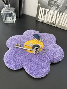 a purple flower shaped rug with two keys on it and a glass vase in the background