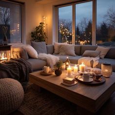 a living room filled with lots of furniture and lit candles in front of large windows