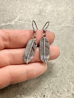 Detailed silver feather dangle earrings. Charm measures approximately 10mm across. Approximately 40mm drop. Stainless steel ear wires. Comes on branded card with clear ear backs. For added flare and style, these feather earrings will take your look to new heights (haha!). With a 10mm charm and 40mm drop, these stainless steel earrings are both chic and durable. Plus, they come with branded cards and clear ear backs for easy storage and wear. Indiana Love, Baby Jewelry, Garden Print, Silver Feather, Steel Earrings, Bag Icon, Print Book, Feather Earrings, Stainless Steel Earrings