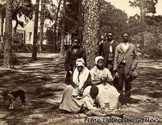 an old black and white photo of people sitting in the woods with a dog nearby