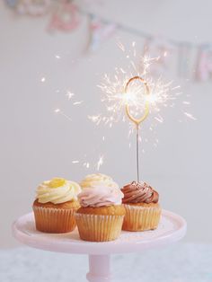 three cupcakes on a cake stand with a sparkler