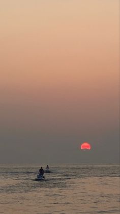 two people on small boats in the ocean at sunset or dawn with red sun behind them