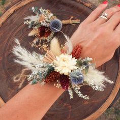 a woman's hand is shown with flowers and feathers on her wrist, sitting on a wooden table