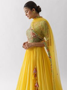 A three-piece sunflower lehenga set from the Suruchi Parakh collection. This beautiful yellow lehenga is paired with a green floral print blouse. The hand-embroidered green blouse has intricate floral bead and sequins detail. The yellow and green color with thread work enhances the graceful georgette crepe lehenga. The lehenga has side hanging triangle tassels to the waistline. The outfit is completed with a yellow dupatta with ruffle borders. Hand Embroidered Blouse, Green Floral Blouse, Yellow Lehenga, Add Sleeves, Embroidered Lehenga, Casual Wear Dress, Embroidered Skirt, Fashion App, Floral Print Blouses