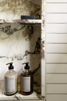 two soap dispensers sitting on top of a marbled shelf next to each other