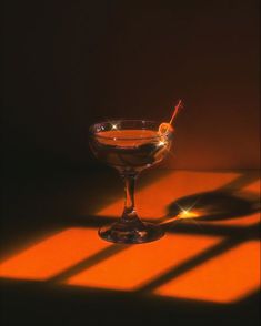 a glass filled with liquid sitting on top of a orange table next to a shadow