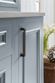 a close up of a door handle on a kitchen cabinet with flowers in the background