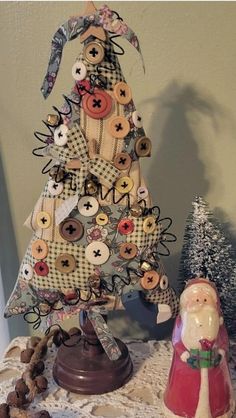 a christmas tree made out of buttons and other items on a table next to a small figurine