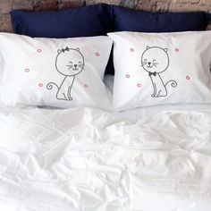 two pillows with cats drawn on them sitting on a bed in front of a brick wall