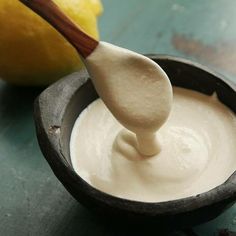 a wooden spoon in a small bowl filled with white sauce next to a lemon on a table