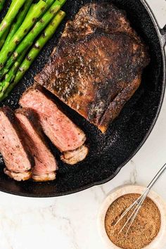 steak, asparagus and seasoning in a skillet on a marble counter