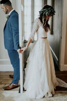 a man and woman standing next to each other in front of an open door wearing wedding dresses