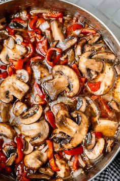 mushrooms and peppers cooking in a skillet on a stove top with a checkered cloth