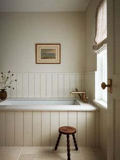 a bath tub sitting next to a window with a painting on the wall above it