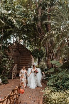 two brides holding hands walking through the woods at their outdoor wedding venue in florida