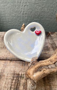 a ceramic heart shaped dish with a red nose on it sitting on a piece of driftwood