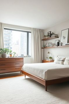 a bedroom with a bed, dresser and window in front of the cityscape