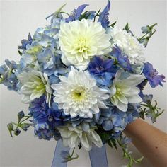 a bouquet of blue and white flowers is held up by a person's hand