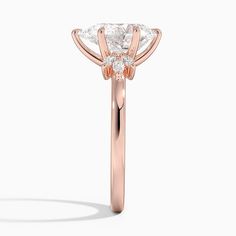 a rose gold engagement ring with two pear shaped diamonds on the side and an oval diamond center