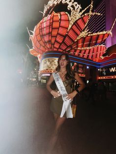 a woman standing in front of a building with a sash around her waist and wearing a tiara