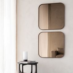 two mirrors on the wall above a small table with a candle in front of it