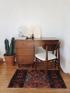 a room with a rug, table and chair next to a potted cacti