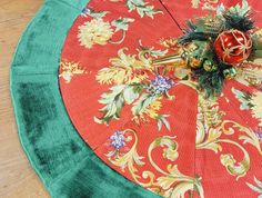 a red and green umbrella with flowers on it sitting on a wooden floor next to a plant