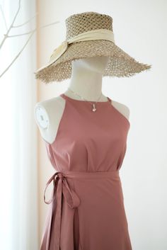 a mannequin wearing a pink dress and large straw hat in front of a window