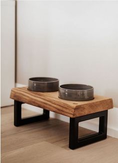 two bowls sit on a wooden bench in front of a white wall and hardwood floor