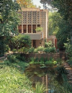 the house is surrounded by greenery and trees, with a pond in front of it