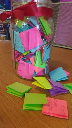 a jar filled with lots of different colored sticky notes on top of a wooden table