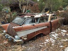 an old rusted out car sitting in the woods