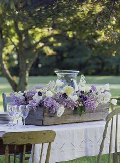 a wooden box filled with flowers sitting on top of a table next to a white table cloth