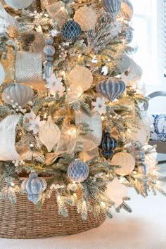 a white christmas tree with blue and silver ornaments in a wicker basket on the floor