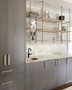 a kitchen with marble counter tops and gold accents on the shelves, along with gray cabinets