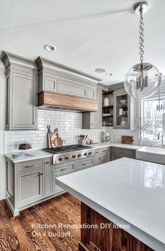 a large kitchen with wooden floors and gray cabinets, white counter tops and wood flooring