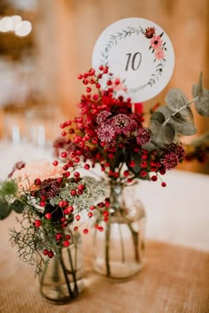 two vases filled with flowers and greenery on top of a burlap table