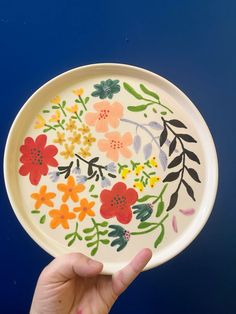 a hand holding a plate with flowers painted on it