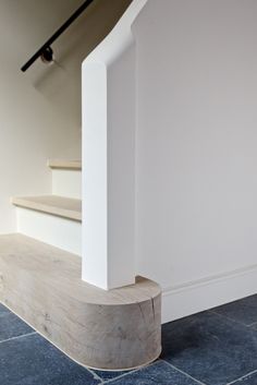 a wooden bench sitting in front of a white wall next to a set of stairs