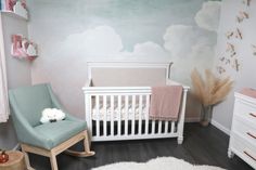 a baby's room with a white crib, blue chair and wall mural