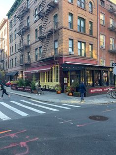 the people are crossing the street in front of the building with fire escapes on it