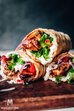 three wraps with chicken, lettuce and tomatoes on them sitting on a cutting board