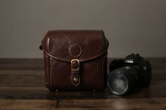 a brown leather camera bag sitting on top of a wooden table next to a digital camera