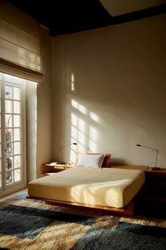 a bed sitting next to a window on top of a wooden dresser under a lamp