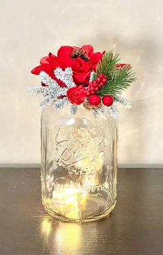 a glass jar filled with red flowers and greenery