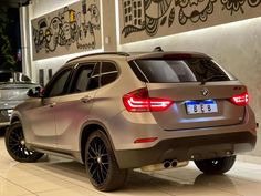 the rear end of a silver bmw suv parked in front of a wall with graffiti on it