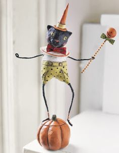 a black cat figurine holding a candy cane on top of a small pumpkin